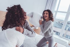 Курчавые милые девушки чувствуя смешной имеющ сражение подушки стоковые изображения rf Курчавые милые девушки чувствуя смешной имеющ сражение подушки стоковые изображения rf