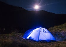Ландшафт горы ночи с загоренным голубым шатром Горные пики и луна на открытом воздухе на озере Lacul Balea, Transfagarasan, стоковые фото Ландшафт горы ночи с загоренным голубым шатром Горные пики и луна на открытом воздухе на озере Lacul Balea, Transfagarasan, стоковые фото