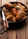 Лоток с зажаренными картошками и зажаренными сосисками, зеленым розмариновым маслом, вилкой и ножом стоковая фотография Лоток с зажаренными картошками и зажаренными сосисками, зеленым розмариновым маслом, вилкой и ножом стоковая фотография