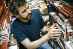Любознательная книга чтения человека между полками в библиотеке стоковое изображение rf Любознательная книга чтения человека между полками в библиотеке стоковое изображение rf