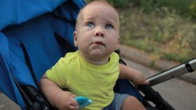 Любознательный младенческий мальчик сидя в pram outdoors Любознательный младенческий мальчик сидя в pram outdoors