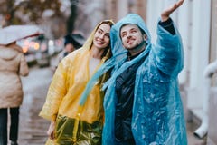 Любя парень и девушка в желтых и голубых плащах идут на улицу в дожде стоковая фотография rf Любя парень и девушка в желтых и голубых плащах идут на улицу в дожде стоковая фотография rf