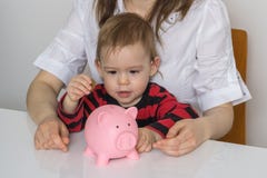 Маленькая девочка кладет монетки в piggy банк денег и собирает сбережения стоковая фотография Маленькая девочка кладет монетки в piggy банк денег и собирает сбережения стоковая фотография