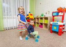 Мальчик и девушка играют с прогулочной коляской игрушки дома стоковые изображения rf Мальчик и девушка играют с прогулочной коляской игрушки дома стоковые изображения rf