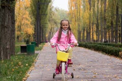 Маленькая девочка в розовом плаще и резиновые ботинки едет bi стоковые изображения rf Маленькая девочка в розовом плаще и резиновые ботинки едет bi стоковые изображения rf