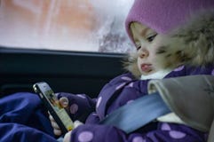 Маленькая девочка играет в телефоне пока сидящ в автомобиле в месте ребенка стоковая фотография Маленькая девочка играет в телефоне пока сидящ в автомобиле в месте ребенка стоковая фотография