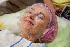 Маленькая девочка лежит на кресле во время косметических процедур с маской на сторонах над которыми beautician наводит стоковое изображение rf Маленькая девочка лежит на кресле во время косметических процедур с маской на сторонах над которыми beautician наводит стоковое изображение rf