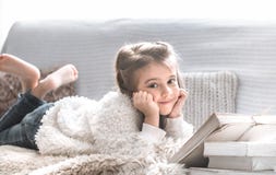 Маленькая девочка читая книгу на удобной софе, красивых эмоциях стоковое фото rf Маленькая девочка читая книгу на удобной софе, красивых эмоциях стоковое фото rf