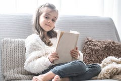 Маленькая девочка читая книгу на удобной софе, красивых эмоциях стоковая фотография Маленькая девочка читая книгу на удобной софе, красивых эмоциях стоковая фотография