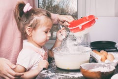 Маленькая милая девушка и ее мать подготавливая тесто в кухне дома стоковые изображения rf Маленькая милая девушка и ее мать подготавливая тесто в кухне дома стоковые изображения rf