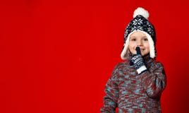 Мальчик ребенка в связанной шляпе и свитере и mittens делая для того чтобы заставить замолчать жест над красочной красной предпос стоковая фотография rf Мальчик ребенка в связанной шляпе и свитере и mittens делая для того чтобы заставить замолчать жест над красочной красной предпос стоковая фотография rf