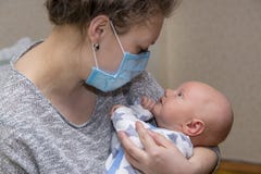 Мама, которая больна, держит ее младенца в защитной медицинской маске Стоковые Фотографии RF Мама, которая больна, держит ее младенца в защитной медицинской маске Стоковые Фотографии RF