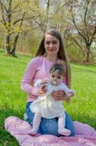 Мама с младенцем в ярких одеждах на розовой шотландке на зеленом праве Семья отдыхая в парке на теплый день стоковая фотография rf Мама с младенцем в ярких одеждах на розовой шотландке на зеленом праве Семья отдыхая в парке на теплый день стоковая фотография rf