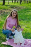 Мама с младенцем в ярких одеждах на розовой шотландке на зеленом праве Семья отдыхая в парке на теплый день стоковые фотографии rf Мама с младенцем в ярких одеждах на розовой шотландке на зеленом праве Семья отдыхая в парке на теплый день стоковые фотографии rf