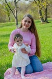 Мама с младенцем в ярких одеждах на розовой шотландке на зеленом праве Семья отдыхая в парке на теплый день стоковое изображение rf Мама с младенцем в ярких одеждах на розовой шотландке на зеленом праве Семья отдыхая в парке на теплый день стоковое изображение rf
