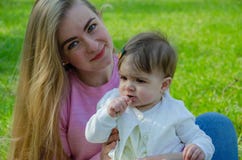 Мама с младенцем в ярких одеждах на розовой шотландке на зеленом праве Семья отдыхая в парке на теплый день стоковая фотография Мама с младенцем в ярких одеждах на розовой шотландке на зеленом праве Семья отдыхая в парке на теплый день стоковая фотография