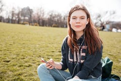 Милая женщина слушая к музыке от мобильного телефона на лужайке Стоковые Фотографии RF Милая женщина слушая к музыке от мобильного телефона на лужайке Стоковые Фотографии RF