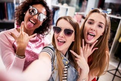 Милые девушки нося солнечные очки околпачивая вокруг принимать selfie показывая жесты языка и рожка в одежде ходят по магазинам стоковые фотографии rf Милые девушки нося солнечные очки околпачивая вокруг принимать selfie показывая жесты языка и рожка в одежде ходят по магазинам стоковые фотографии rf