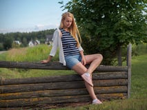 Милая белокурая женщина представляя на старое деревянном обнести шорты джинсовой ткани Стоковая Фотография Милая белокурая женщина представляя на старое деревянном обнести шорты джинсовой ткани Стоковая Фотография