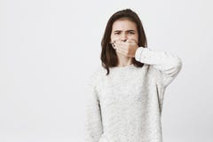 Милая девушка брюнет покрывает ее рот и выражает отвращение или нелюбовь, хмурится брови, над белой предпосылкой Молодые стоковое фото rf Милая девушка брюнет покрывает ее рот и выражает отвращение или нелюбовь, хмурится брови, над белой предпосылкой Молодые стоковое фото rf