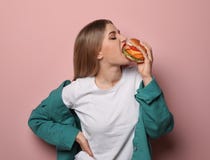 Милая женщина есть вкусный бургер на предпосылке цвета стоковые изображения Милая женщина есть вкусный бургер на предпосылке цвета стоковые изображения
