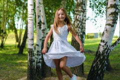 Милая маленькая девочка в белых водоворотах и танцах платья среди деревьев стоковые изображения rf Милая маленькая девочка в белых водоворотах и танцах платья среди деревьев стоковые изображения rf