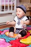 Милый младенец в striped рубашке и шляпах усаженных на циновку в комнате стоковая фотография rf Милый младенец в striped рубашке и шляпах усаженных на циновку в комнате стоковая фотография rf