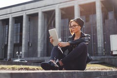 Модно одетая девушка битника в связанной шляпе использует электронную таблетку сидя снаружи в городе стоковое фото Модно одетая девушка битника в связанной шляпе использует электронную таблетку сидя снаружи в городе стоковое фото