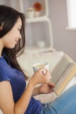 Молодая азиатская женщина сидя на софе читая книгу держа ее Стоковое фото RF Молодая азиатская женщина сидя на софе читая книгу держа ее Стоковое фото RF