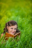 Молодая женщина лежа на траве и книге чтения стоковые изображения Молодая женщина лежа на траве и книге чтения стоковые изображения