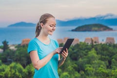 Молодая женщина наслаждается таблеткой на предпосылке моря стоковые фотографии rf Молодая женщина наслаждается таблеткой на предпосылке моря стоковые фотографии rf