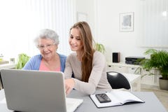 Молодая женщина помогая старой старшей женщине делая обработку документов и административные процедуры с портативным компьютером стоковое фото Молодая женщина помогая старой старшей женщине делая обработку документов и административные процедуры с портативным компьютером стоковое фото