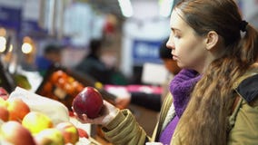 Молодая, красивая беременная женщина в супермаркете выбирает свежие органические яблока Молодая, красивая беременная женщина в супермаркете выбирает свежие органические яблока