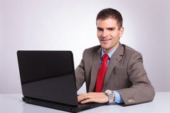 Молодой бизнесмен смотрит вас пока работающ на компьтер-книжке стоковые изображения Молодой бизнесмен смотрит вас пока работающ на компьтер-книжке стоковые изображения