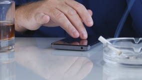 Мобильный телефон пользы BusinessmMan куря сигару и выпивая Alcoholan в офисе используя карманную книжку для записи информации стоковая фотография rf Мобильный телефон пользы BusinessmMan куря сигару и выпивая Alcoholan в офисе используя карманную книжку для записи информации стоковая фотография rf