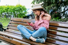 Модно одетая молодая женщина на улице на солнечном вечере Девушка в джинсах, блузке и небольшой шляпе сидит на стенде и стоковые фотографии rf Модно одетая молодая женщина на улице на солнечном вечере Девушка в джинсах, блузке и небольшой шляпе сидит на стенде и стоковые фотографии rf
