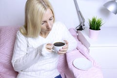 Молодая белокурая женщина сидя на розовой софе и выпивая кофе стоковая фотография rf Молодая белокурая женщина сидя на розовой софе и выпивая кофе стоковая фотография rf