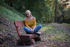 Молодая белокурая женщина сидя самостоятельно на деревянной скамье в лесе, унылый и сиротливый стоковое изображение Молодая белокурая женщина сидя самостоятельно на деревянной скамье в лесе, унылый и сиротливый стоковое изображение