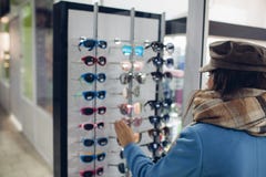 Молодая женщина в оптически магазине - красивая девушка выбирает стекла в магазине optician стоковые изображения rf Молодая женщина в оптически магазине - красивая девушка выбирает стекла в магазине optician стоковые изображения rf
