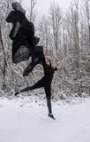 Молодая женщина в черном костюме балета скача в снежный лес с черной тканью в воздухе стоковые фото Молодая женщина в черном костюме балета скача в снежный лес с черной тканью в воздухе стоковые фото