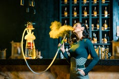 Молодая женщина куря кальян за баром Облако дыма Портрет красоты молодой женщины наслаждаясь кальяном стоковые фотографии rf Молодая женщина куря кальян за баром Облако дыма Портрет красоты молодой женщины наслаждаясь кальяном стоковые фотографии rf