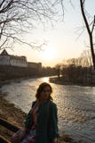 Молодая женщина моды ослабляя и наслаждаясь заход солнца около реки в стоковое изображение Молодая женщина моды ослабляя и наслаждаясь заход солнца около реки в стоковое изображение