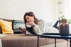 Молодая женщина ослабляя в живущей комнате используя смартфон и выпивая кофе r стоковые фото Молодая женщина ослабляя в живущей комнате используя смартфон и выпивая кофе r стоковые фото