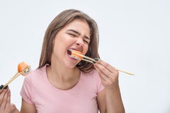 Молодая женщина пожирает части суш Она сдерживает часть Модель держит их с палочками Изолировано на серой предпосылке стоковое фото rf Молодая женщина пожирает части суш Она сдерживает часть Модель держит их с палочками Изолировано на серой предпосылке стоковое фото rf