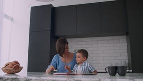 Молодая испанская мать с ее сыном сидя на таблице учит для чтения ребенка помогая и пробуждая его сына, видеоматериал Молодая испанская мать с ее сыном сидя на таблице учит для чтения ребенка помогая и пробуждая его сына, видеоматериал