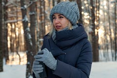 Молодая красивая блондинка в напитках кофе или чае связанной шляпы, шарфа и перчаток в лесе зимы покрытом снег на заходе солнца стоковое фото Молодая красивая блондинка в напитках кофе или чае связанной шляпы, шарфа и перчаток в лесе зимы покрытом снег на заходе солнца стоковое фото