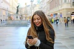 Молодая красивая женщина нося случайные одежды зимы используя телефон на открытом воздухе в европейском городе Девушка с мобильны стоковое изображение Молодая красивая женщина нося случайные одежды зимы используя телефон на открытом воздухе в европейском городе Девушка с мобильны стоковое изображение
