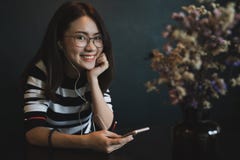 Молодая красивая женщина с умным телефоном, жизнерадостная молодая женщина используя smartphone с наушниками над черной предпосыл стоковая фотография Молодая красивая женщина с умным телефоном, жизнерадостная молодая женщина используя smartphone с наушниками над черной предпосыл стоковая фотография