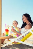 Молодая красивая мать и ее маленькая дочь на пляже, имеющ потеху Девушки выпивают коктеиль Стоковое Изображение RF Молодая красивая мать и ее маленькая дочь на пляже, имеющ потеху Девушки выпивают коктеиль Стоковое Изображение RF