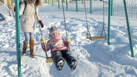 Молодая мать при ребенок отбрасывая на внешнем качания установленное в парке зимы Снег падая, снежности, зимнее время Молодая мать при ребенок отбрасывая на внешнем качания установленное в парке зимы Снег падая, снежности, зимнее время